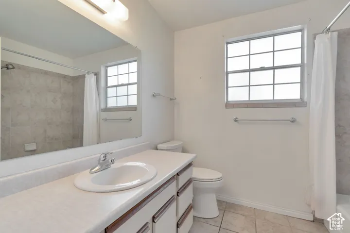 Vanity with integrated sink, tile flooring, window with grid pattern, overhead lighting, and tiled shower surround