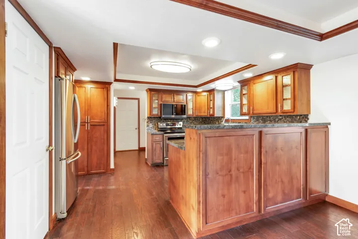 Spacious kitchen featuring wood-finish flooring, abundant wood cabinetry, integrated stainless steel appliances, and solid surface countertops