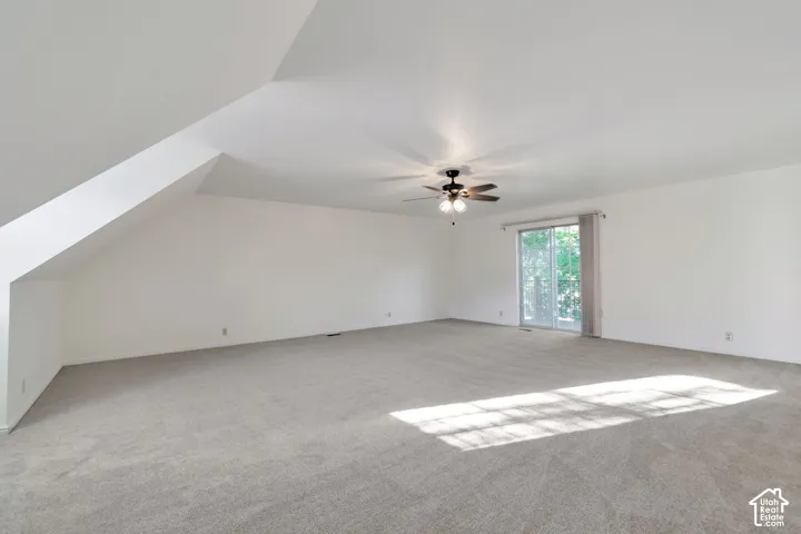 Spacious room featuring sloped ceilings, light-toned carpeting, a ceiling fan, and sliding glass doors