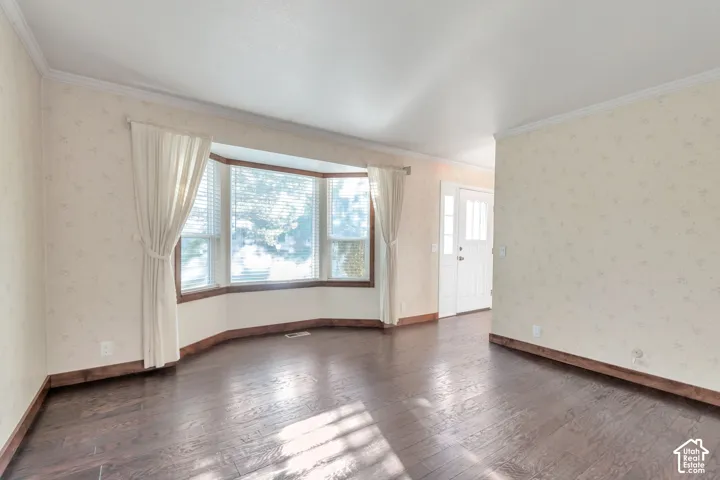 Hardwood-style flooring, bay window with blinds, front entry door with side lights, patterned wallpaper, and crown molding