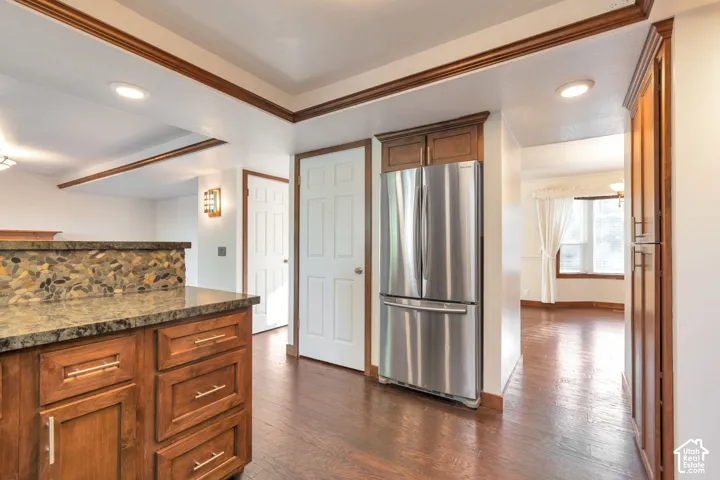 Kitchen featuring wood-finish cabinetry, stone countertop, integrated stainless steel refrigerator, and wood-finish flooring