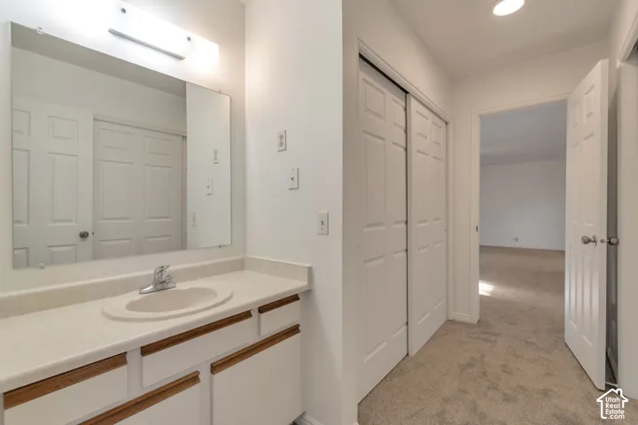Vanity with integrated sink, wall-mounted mirror, overhead light fixture, and white cabinetry