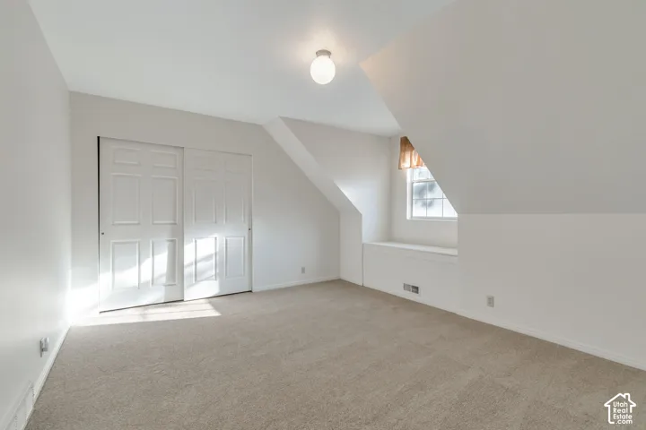 Sliding panel closet doors, neutral wall colors, sloped ceiling design, window with integrated sill, and carpeted flooring