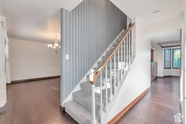 Carpeted staircase with white balusters and wood handrail, wood-finish flooring, white wall molding, and strip-patterned wall covering