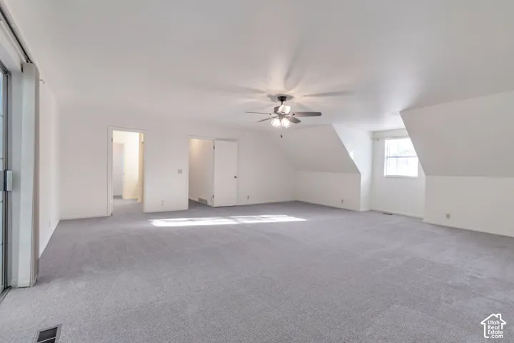Expansive carpeted room featuring a ceiling fan, sloped ceilings, and a window