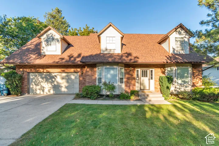 Brick exterior with dormer windows, a two-car garage, and a concrete driveway