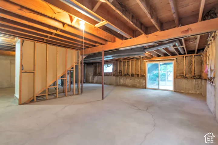 Unfinished basement with exposed ceiling joists and support beams, concrete flooring, framed interior walls, and a sliding glass door