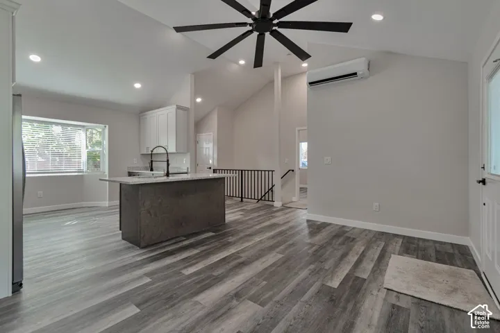 Vaulted ceilings with recessed lighting, wood-finish flooring, kitchen island with integrated sink, white shaker cabinetry, and a wall mounted mini split unit.