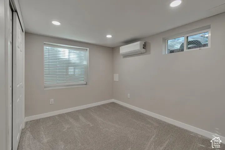 Recessed ceiling lighting, white blinds, individual climate control unit, two windows, and light gray carpeted flooring