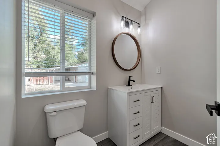 White vanity with granite countertop, cabinet storage, matte black faucet, and oval-framed mirror