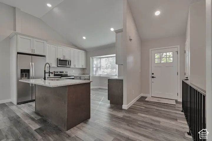 Modern kitchen and entry featuring stainless steel appliances, white cabinetry, Granite countertops, a center island with seating, wood-finish flooring throughout, recessed lighting, and a bright foyer with and black metal railing