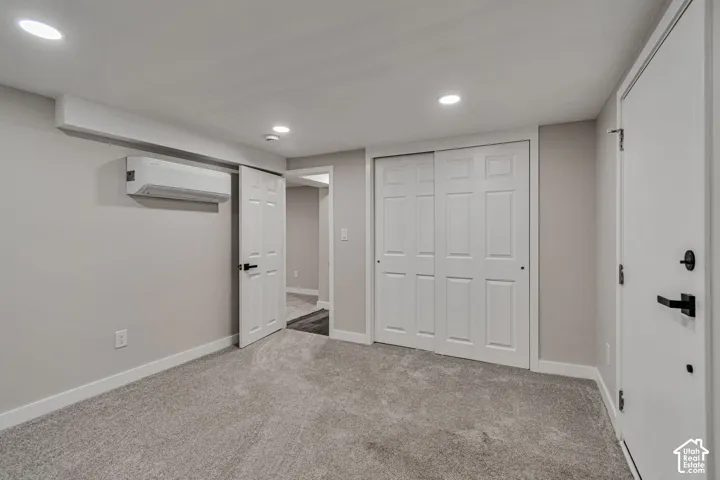 Recessed lighting, light gray wall color, gray carpeting, white paneled doors, and a wall-mounted climate control unit