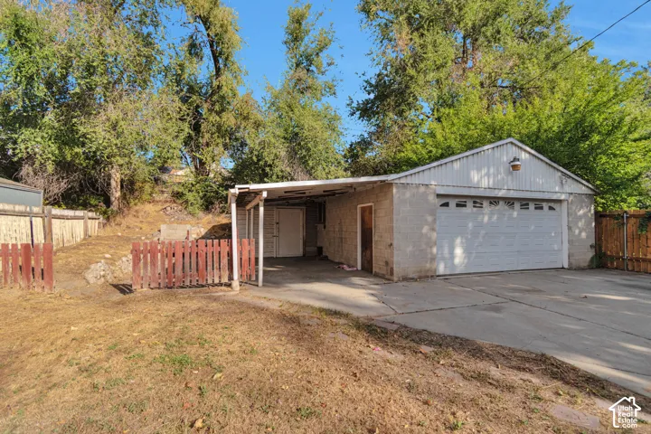 Detached garage with a paneled overhead door, concrete block construction, and an attached carport