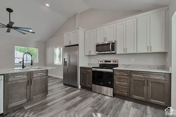 Vaulted ceiling kitchen featuring an island with granite countertops and integrated sink, stainless steel appliances, LVP flooring, and 2 tone cabinetry