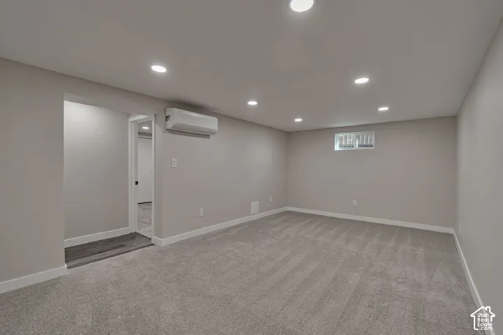 Recessed lighting, light gray carpeting, neutral wall color, white trim, and a wall-mounted climate control unit