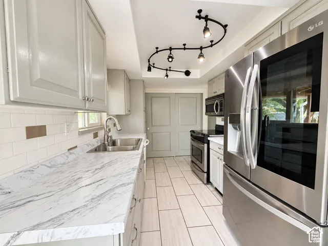 Kitchen featuring light-toned cabinetry, a stainless steel refrigerator, patterned countertops, a subway tile backsplash, and track lighting