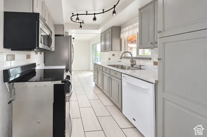 Kitchen featuring light gray cabinetry, white tile flooring, stainless steel appliances, a tile backsplash, and track lighting