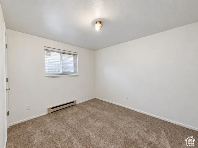 Plush carpet flooring, neutral painted walls, window with horizontal blinds, flush mount ceiling light fixture, and baseboard heating unit
