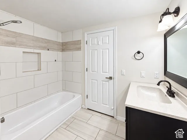 Shower/tub combination with tiled surround, built-in shower niche, solid surface vanity countertop with integrated sink, and black finish fixtures