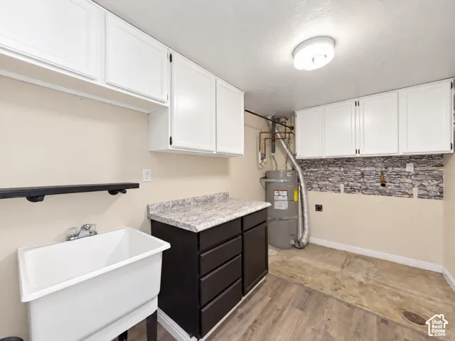 White shaker-style upper cabinetry, laundry sink with a wall-mounted faucet, and wood-finish flooring