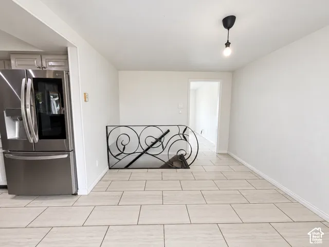 Light-toned tile flooring, stainless steel refrigerator, white wall paint, black wrought iron railing, and a black pendant light fixture
