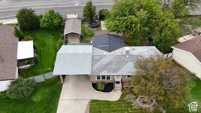 Asphalt shingle roofing, attached carport, concrete driveway, mature landscaping, and shaded front entrance