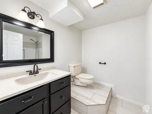 Vanity with dark cabinetry and light countertop, bronze-finish faucet, framed mirror, and overhead lighting fixture