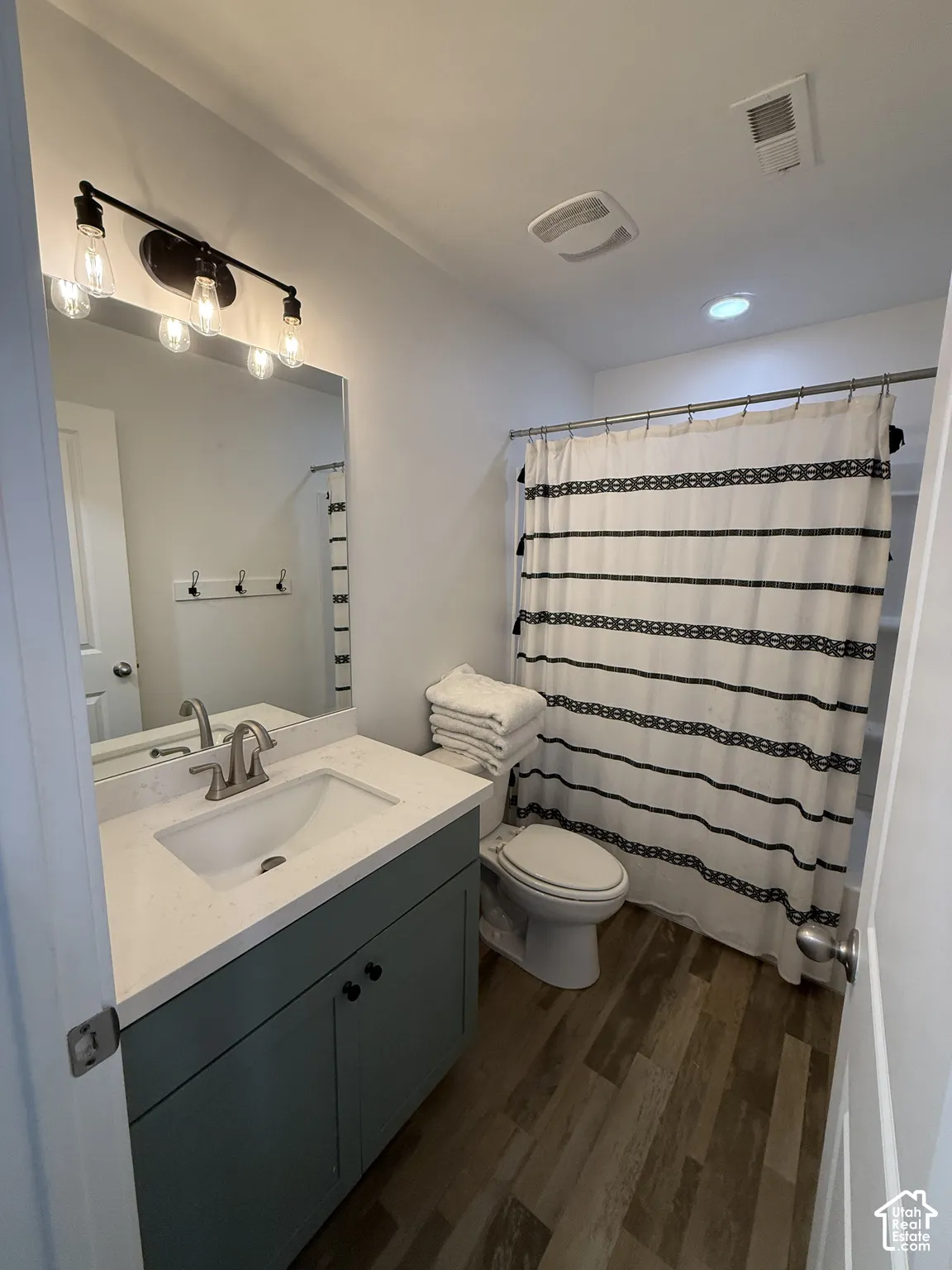 Bathroom featuring wood-finish flooring, a single vanity with a light-colored countertop and undermount sink, and a shower with a curtain rod