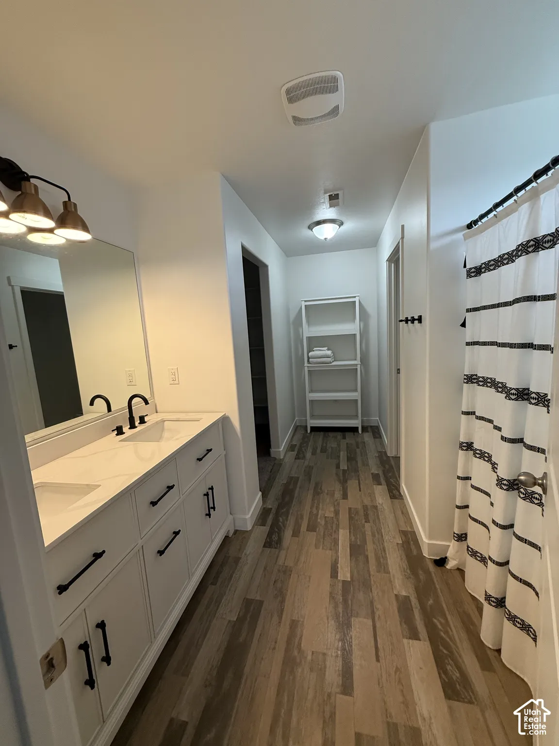 Dual vanity with white cabinetry, wood-finish flooring, and a built-in shower