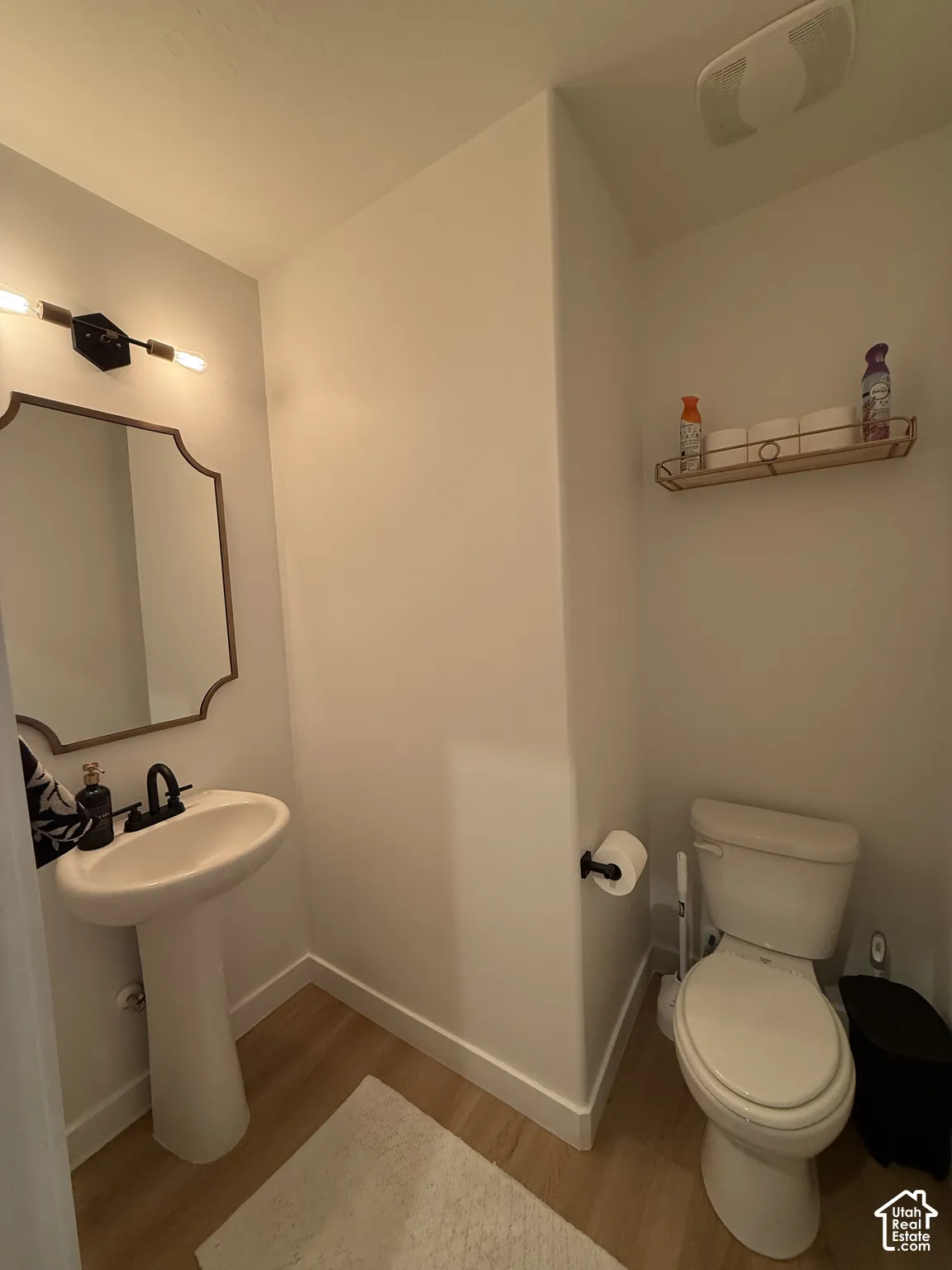 Pedestal sink with a matte black faucet, illuminated by a contemporary vanity light