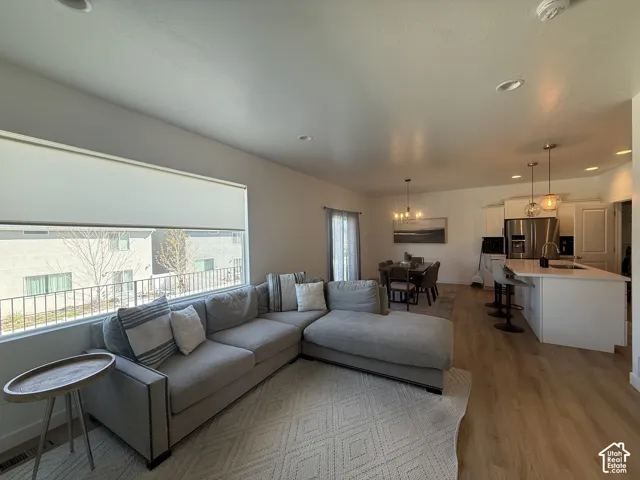 Recessed ceiling lighting, wood-finish flooring, kitchen island with seating, stainless steel appliances, and a dining area with a modern chandelier