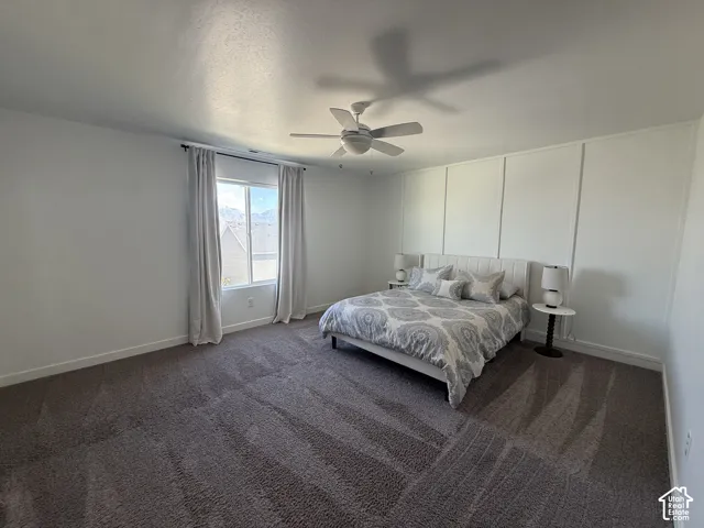 Spacious room featuring broadloom carpeting, a window with a mountain backdrop, a ceiling fan, and an accent wall with vertical paneling