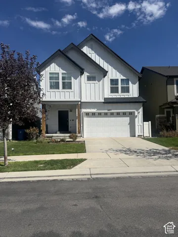 Two-story exterior with board and batten siding, attached garage, concrete driveway, and front lawn
