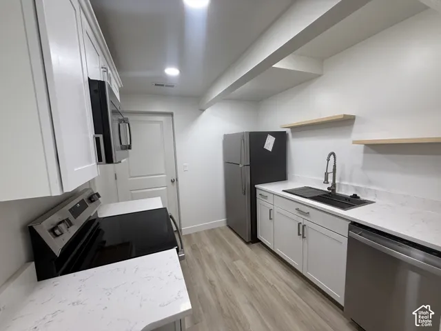 Modern kitchen featuring white shaker cabinetry, stainless steel appliances, light-toned wood-finish flooring, white countertops, and a black sink with a gooseneck faucet