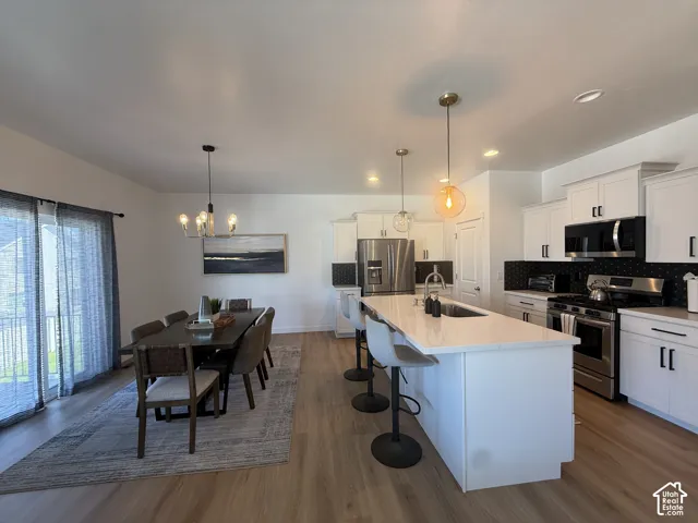 Open-concept living area featuring wood-finish flooring, a kitchen island with seating, stainless steel appliances, white cabinetry with dark hardware, and a sliding glass door