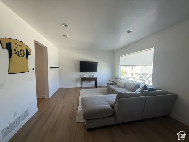 Recessed lighting, wood-finish flooring, and a window with roller shades create a bright living space