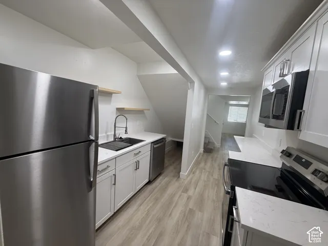 Galley kitchen with white shaker-style cabinetry, stainless steel appliances, quartz countertops, wood-finish flooring, and recessed lighting