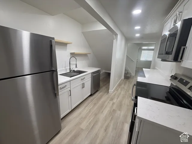 Kitchen featuring stainless steel appliances, white cabinetry, floating wood shelves, and light-toned flooring
