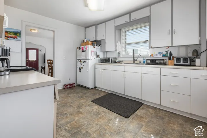 White cabinetry, laminate countertops, single basin stainless steel sink, window with blinds, and durable flooring
