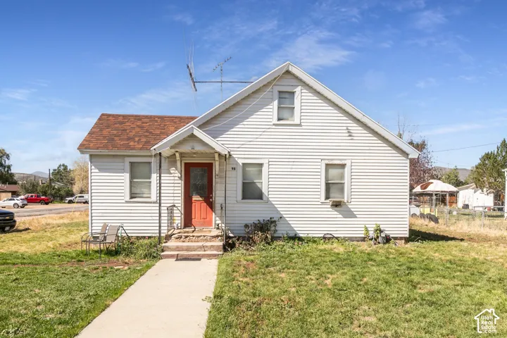 White siding exterior with a brown shingle roof, a red front door, and a concrete pathway leading to the entrance