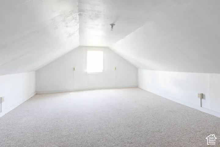 Attic space featuring sloped ceilings, a single window, and light-toned carpeting