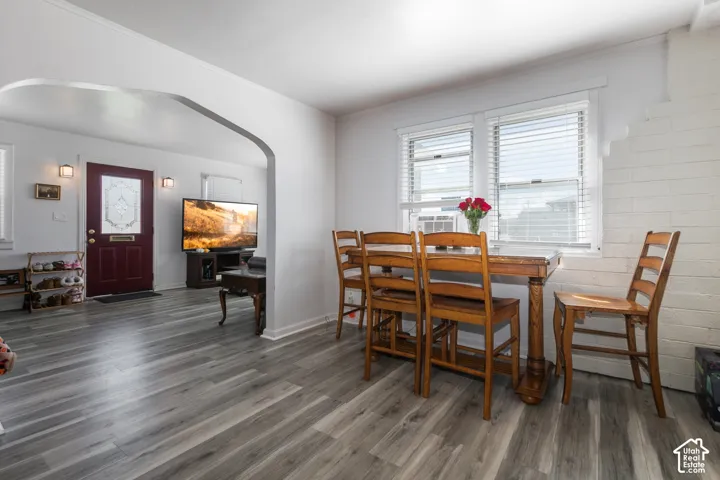 Grey wood-finish flooring throughout, framed doorway archway, white painted brick wall, and double windows with blinds