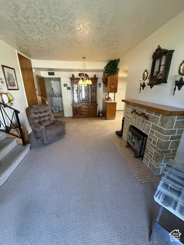Stone-clad fireplace with a wood mantle, carpeted flooring, and a pendant light fixture