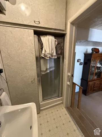White ceramic sink, patterned floor tiling, built-in shower enclosure, upper cabinetry with hardware