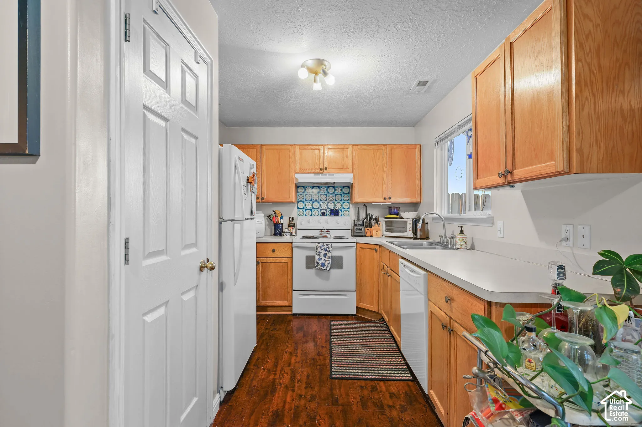 Unit A, Kitchen featuring wood type-finish flooring, light wood cabinetry, white countertops, built-in sink, and white appliances