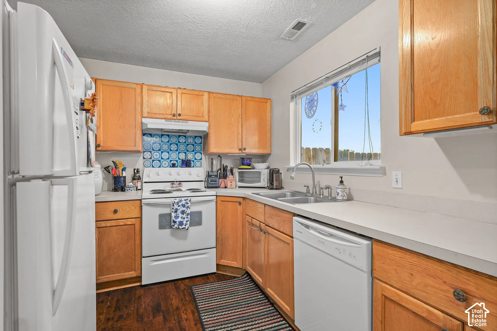 Unit A, Kitchen featuring wood-finish cabinetry, solid surface countertops, a mosaic tile backsplash, a stainless steel sink, and wood-finish flooring