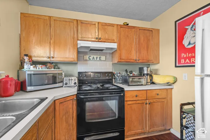 Unit B, Wood-finish cabinetry, light-colored countertops, stainless steel sink, black range, and a tiled backsplash