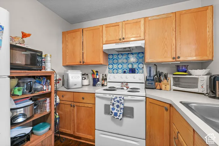 Unit A, Wood-finish cabinetry, light-toned countertops, tile backsplash, white range, and stainless steel sink