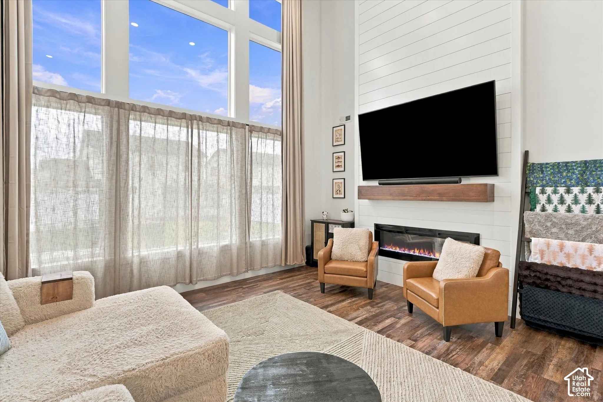 Two-story windows, full-height sheer drapery, shiplap-clad fireplace wall, electric fireplace, and wood-finish flooring