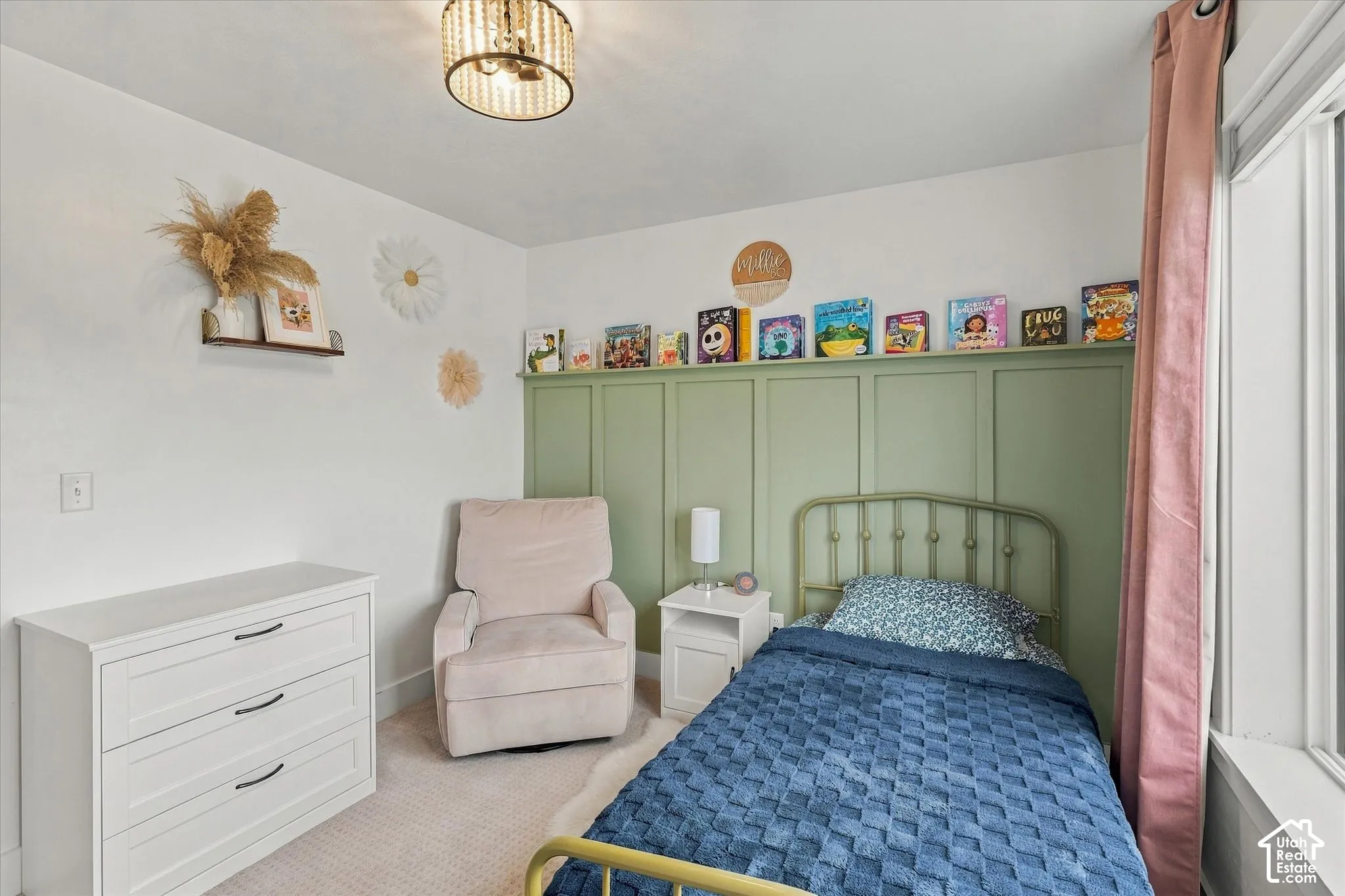 White walls with a contrasting green accent wall featuring paneling, a ceiling-mounted light fixture, white wood-finish dresser with dark hardware, and carpet flooring